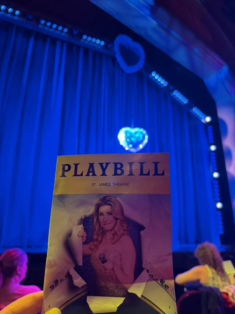 Titanique Playbill held up in front of a blue curtain with glowing heart lights at the St. James Theatre