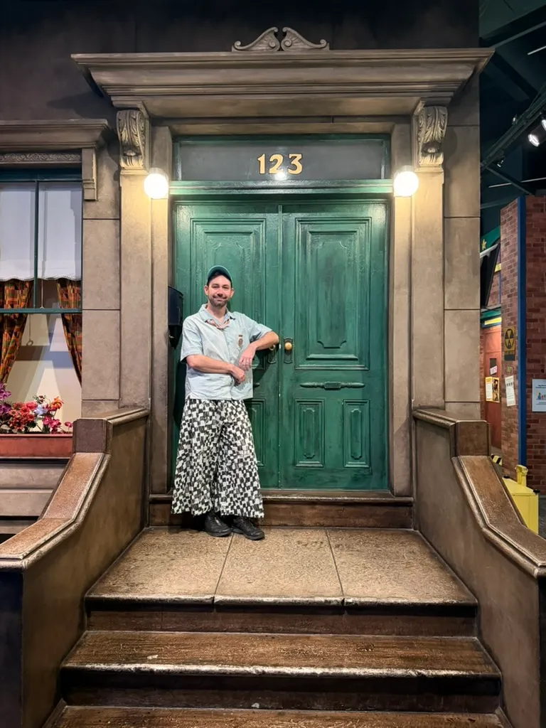 Keith leaning against the green door of 123 Sesame Street on the museum's set, in checkered pants