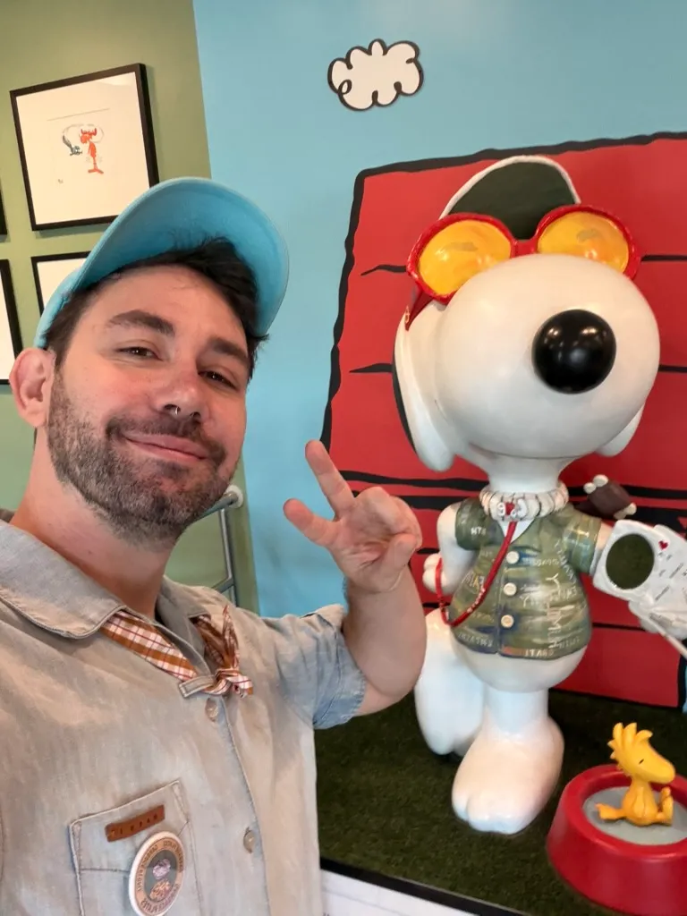 Keith throwing a peace sign next to a statue of Snoopy in red sunglasses and a camo jacket, with Woodstock in his dog bowl